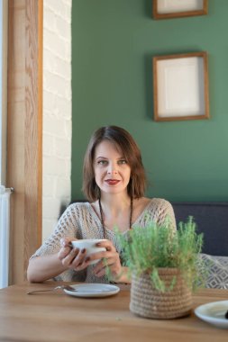 Genç ve başarılı bir kadın kahve masasında kahve ve kahveyle oturuyor ve gülümsüyor. Kahvaltı zamanı..