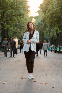 Full-length portrait of stylish young girl in casual style walking in the park. Vertical frame