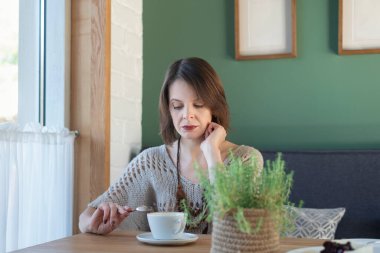 Lonely brooding woman sits at table in cafe. Middle-aged woman drinks coffee or tea in coffee shop