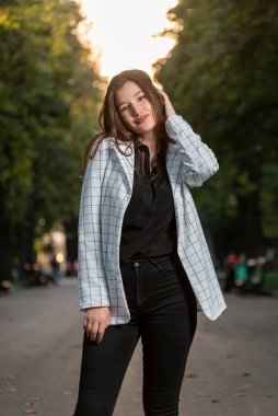 Portrait of cute student girl on park background. Young attractive woman in plaid jacket