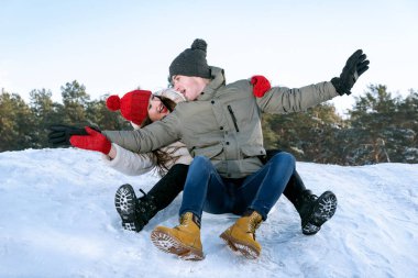 Young happy smiling couple slide down the snow slide against the background of the forest and the blue sky