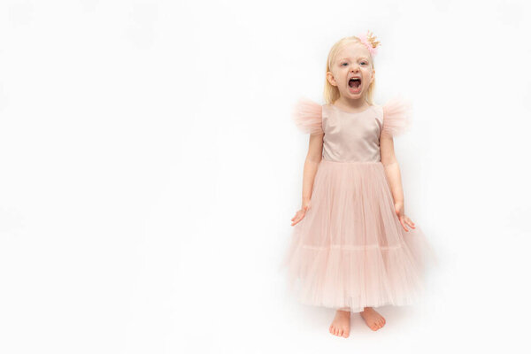Little girl in pink lush dress is screaming . Cute girl in elegant dress and bare feet isolated on white background. Capricious girl.