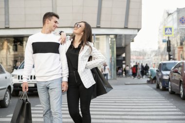 Yolda gülen genç bir çift. Alışveriş yaptıktan sonra ellerinde alışveriş torbalarıyla adam ve kız.