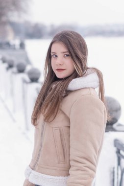 Şık bej renkli koyun derisi ceketli güzel bir genç kadının portresi. Kış yürüyüşü. Şık giyinmiş genç bir kadın..