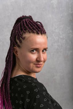 Attractive young woman with pink dreadlocks looks with a smirk. Pretty girl. Portrait of hipster style. Vertical frame