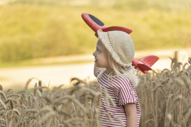 Four-year-old child in straw hat is playing with toy plane in the middle of wheat field. Concept of flights with children