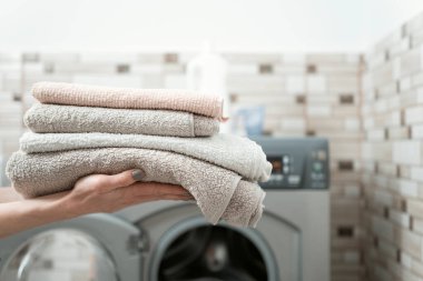 Womens hands hold dry and clean terry towels on the washing machine background. Washing towels