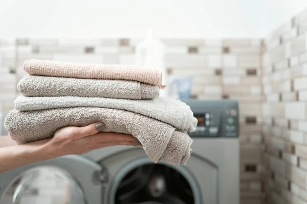 Womens hands hold dry and clean terry towels on the washing machine background. Washing towels