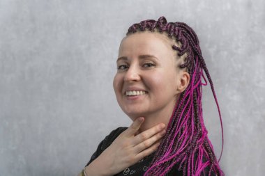 Portrait of cheerful young caucasian woman with pink artificial dreadlocks on gray background