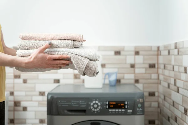 Womens hands hold terry towels on the washing machine background. Washing towels