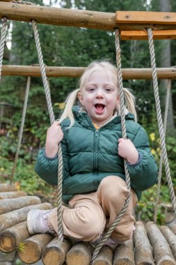 Sonbaharda asma köprüde ya da oyun bahçesinde iki at kuyruklu ve sıcak yeşil ceketli şirin bir kızın dikey portresi.