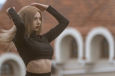 Uzun sarı saçlı, çekici bir kadının portresi siyah bluz giyer ve saçını düzeltir.