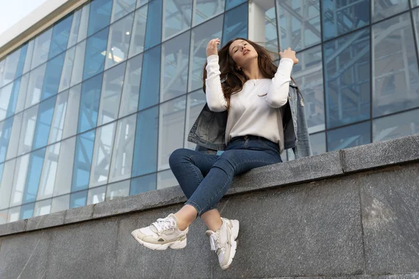 stock image Stylish student girl resting inside and straightening her hair. Beautiful student girl on summer city street.