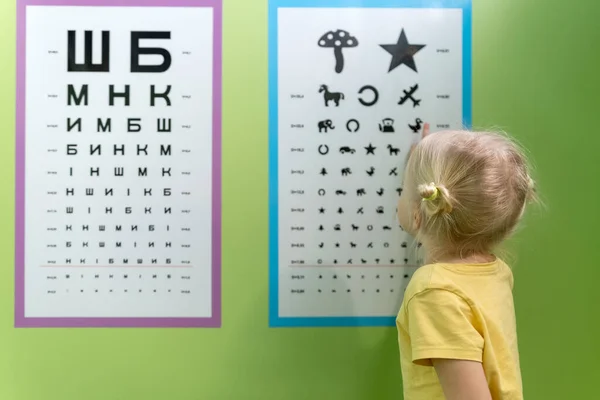 Little girl at appointment with optometrist near poster to check her eyesight. Pediatric optometrist for prescooler.