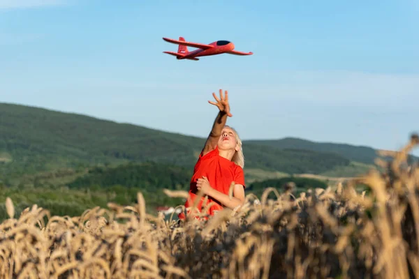 Happy boy launch model airplane into the sky. Happy carefree childhood.Red toy plane against blue sky.