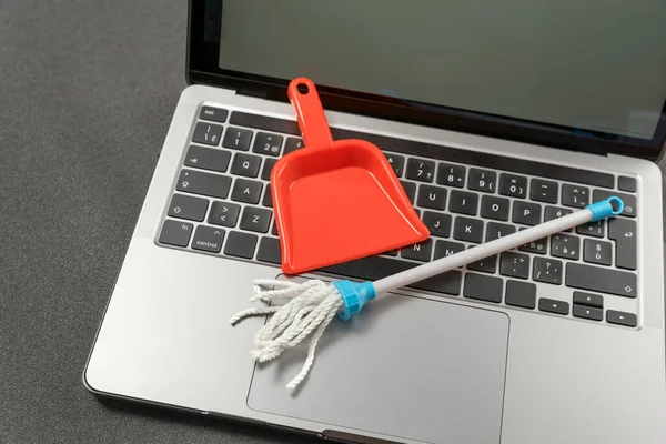 Laptop cleaning concept. Small toy shovel and mop on laptop keyboard. Online cleaning service.