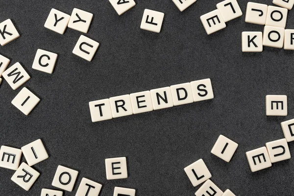 White cubes make up the words TRENDS surrounded by chaotic alphabet letters on gray background. Popular and relevant topics. Monitoring new business opportunities