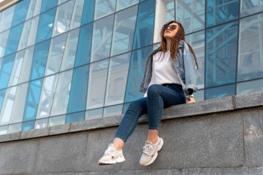 Şehir caddesinde güneşsiz bir şekilde çekici bir kadın dinleniyor. Şehir sokaklarında genç bir kadın var.