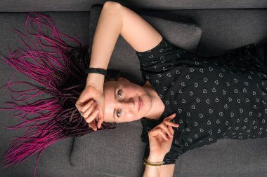 Rastgele giyinmiş beyaz kadın portresi. Rastgele kameraya bakıyor ve kanepede uzanıyor.