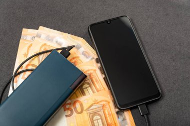 Elektrik bankası, akıllı telefon ve kağıt para. Gri arka planda nakit para. Cihaz alımı. Güç tasarrufu aygıtı ve telefon.