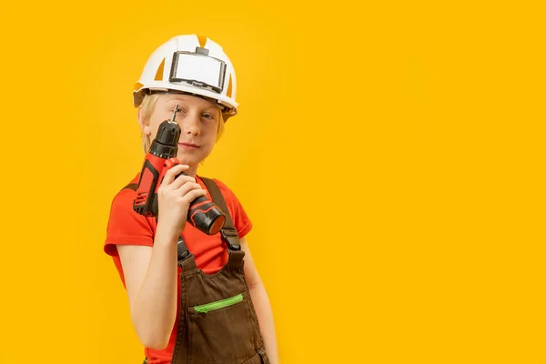 10岁的男孩在黄色背景下孤立地模仿建筑工人 孩子们戴着头盔 干活的人手里拿着钻头 — 图库照片