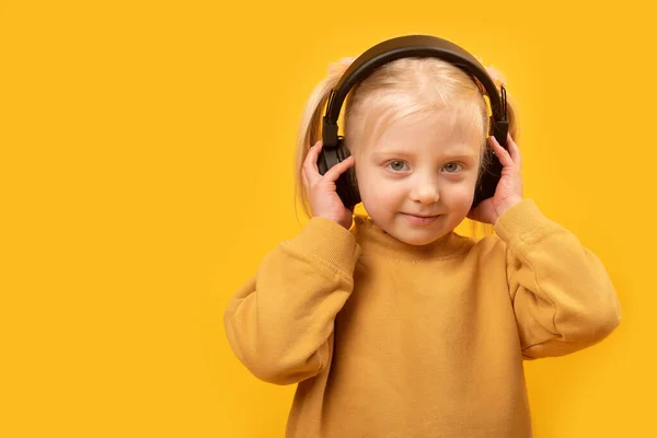 黄色の背景にヘッドフォンを持つ若いフェアヘアの女の子 子供はヘッドフォンで音楽を聴くのが好きだ — ストック写真