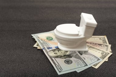 Küçük oyuncak beyaz klozet nakit dolarların üzerinde duruyor. Evdeki tesisatı yenilemek ya da tamir etmek.