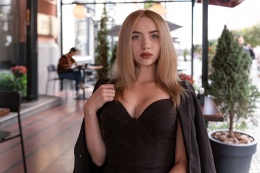Kafede yakalı, sarı saçlı, siyah takım elbiseli seksi genç bir kadının portresi kameraya bakıyor.