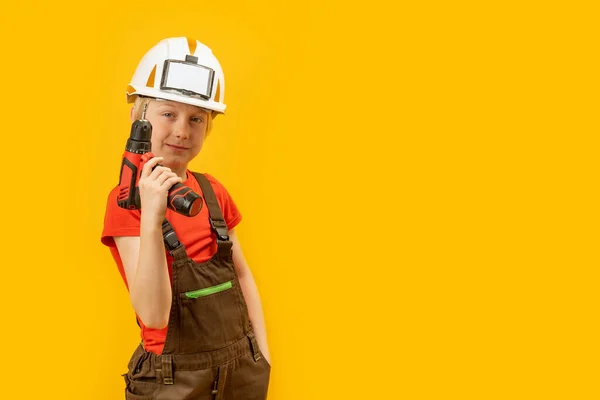 孩子们戴着头盔 工作服手里拿着钻头 10岁的男孩子模仿建筑工人 在黄色背景下与世隔绝 — 图库照片