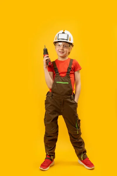 身穿工作服 头戴防护头盔的十几岁男孩正在操练 小孩就像黄色背景的建筑工人 — 图库照片