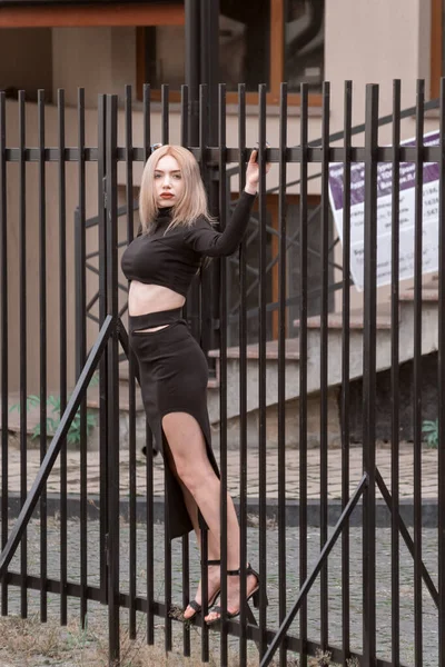 Blondynka Modelka Obcisłych Czarnych Ciuchach Pozuje Pobliżu Czarnego Metalowego Ogrodzenia — Zdjęcie stockowe