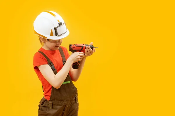 Boy in image of builder worker in white protective helmet using drill isolated on yellow background. Copy space
