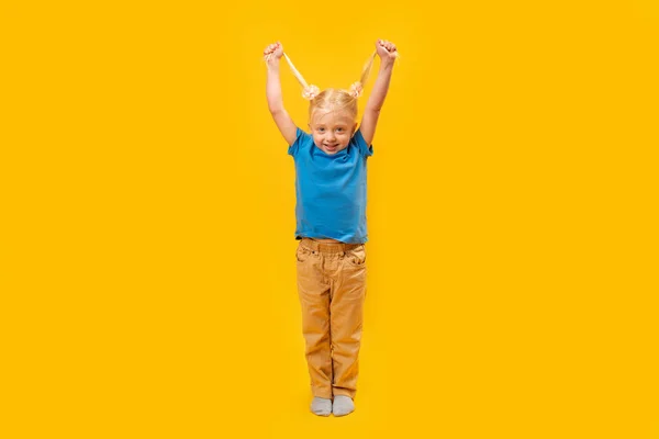 有两个马尾辫的笑着小女孩的全长肖像 穿着黄色背景的蓝色T恤快乐的学龄前儿童 — 图库照片