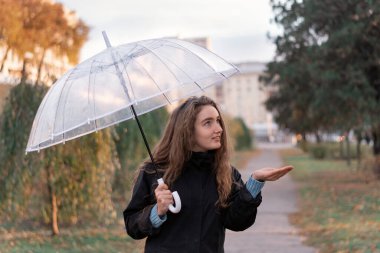 Bulutlu bir sonbahar gününde şemsiyeli bir kız. Uzun kahverengi saçlı, elinde şemsiyeyle dışarıda duran genç bir kadının portresi.