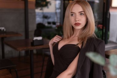 Koyu yakalı siyah elbiseli şık genç kadın kafede oturuyor. Kafeteryadaki seksi sarışın manken.