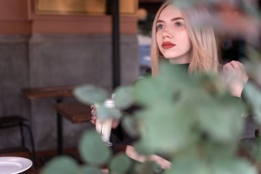 Kafede yalnız başına dalgın güzel bir kız. Çekici sarışın kadın kahve dükkanında bir fincan kapuçino kahvesi ile oturuyor.