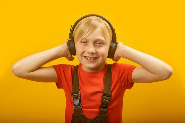 ヘッドフォンで音楽を聴きながら 色白の髪の男の子の笑顔 子供はヘッドフォンで手を置きカメラを見て — ストック写真