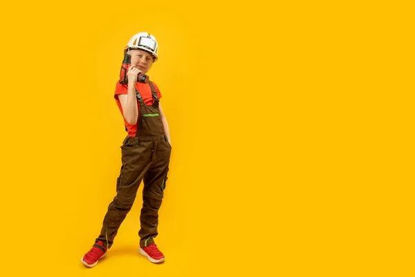 男孩戴着头盔 工作服手里拿着钻头 10岁儿童模仿建筑工人 黄种人背景 复制空间 — 图库照片