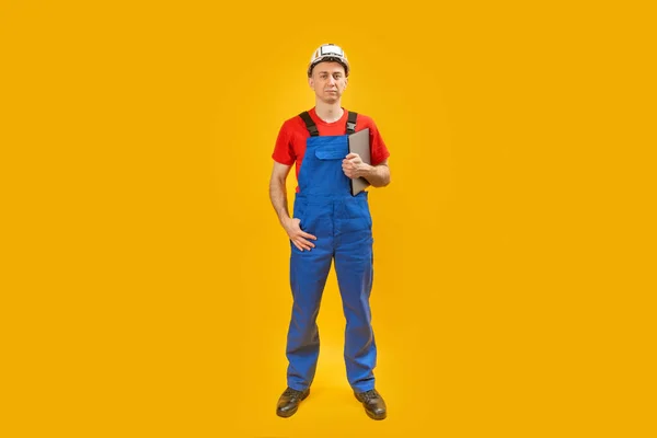 穿着工作服 头戴硬礼帽的男性工程师拿着剪贴板 看着被黄色背景隔离的相机 复制空间 — 图库照片