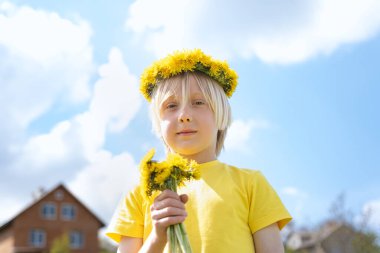 Sarı tişörtlü, çiçekli ve mavi gökyüzü ve evlere karahindiba demetli sarı saçlı çocuk. Mutlu bir çocukluk. Savaşsız bir dünya