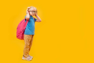 Stüdyo boyunda, sarı arkaplanlı, okul için sırt çantası takan sarışın bir kız. Boşluğu kopyala.