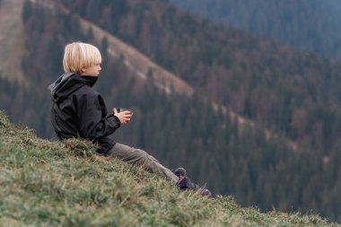 Sarışın genç çocuk bir fincan çayla yamaçta oturur. Çocuk dağlarda dinleniyor. Gezintiye çıkıyorum.