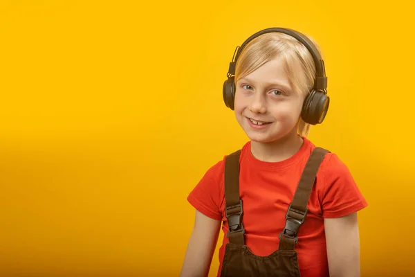 黄色の背景にヘッドフォンでブロンドの少年の肖像画 子供は笑顔で音楽に耳を傾け カメラを見つめます スペースのコピー — ストック写真