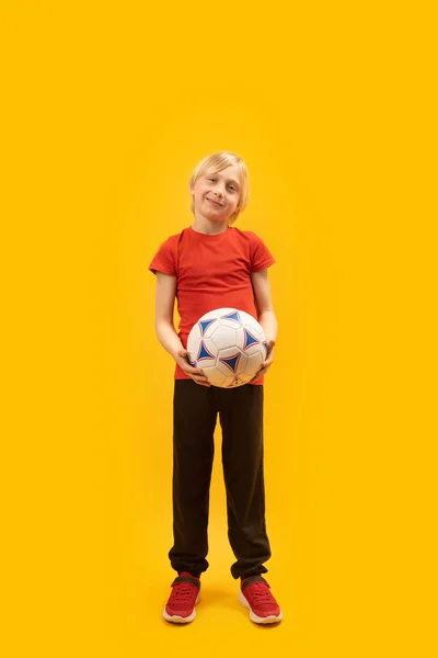 全长的金发碧眼的学生画像 穿着红色T恤 手里拿着足球 笑笑的男生足球运动员 — 图库照片