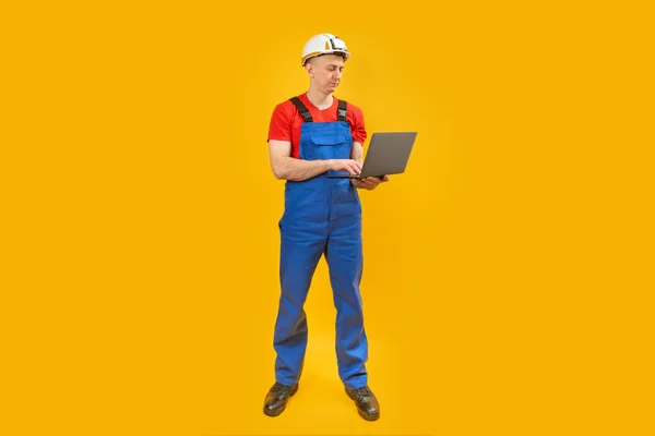 男子工程师或工人站在笔记本电脑黄色背景 全长肖像 蓝色工作服的建筑师 复制空间 — 图库照片
