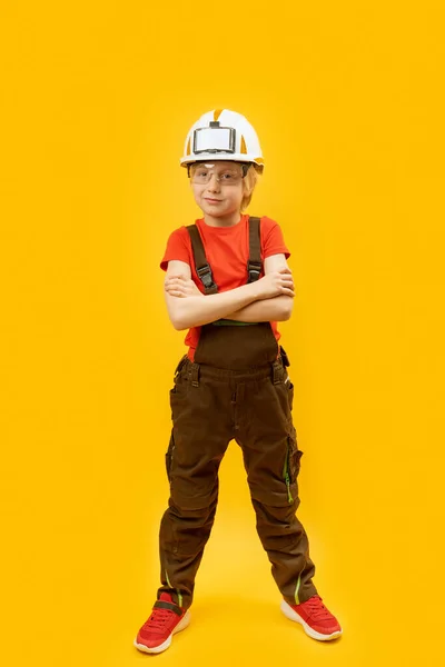 小男孩模仿戴着头盔和工作服的工人 儿童在黄色背景下作为建设者的肖像 复制空间 — 图库照片