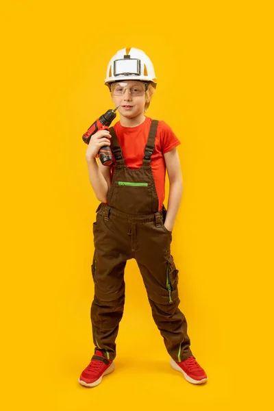 工事全体での建設労働者の役割の少年の垂直フレームの肖像画と彼の手のドリルでヘルメット 職業の選択 — ストック写真