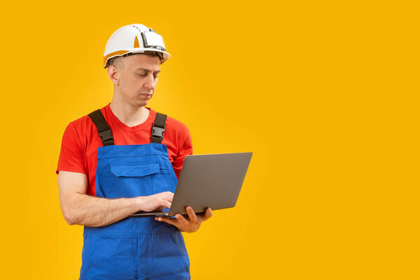 Male industrial engineer or worker standing with laptop on yellow background in photo studio. Copy space