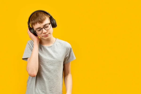 音楽やオーディオブックやオーディオレッスンを聞きながら 彼の頭の上にヘッドフォンで眼鏡をかけて十代のブルネットの少年の肖像画 スペースのコピー — ストック写真