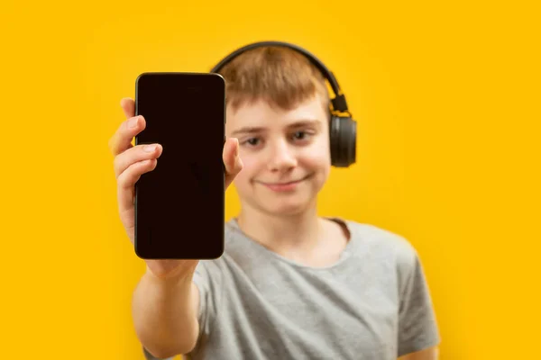 学校の男の子の手の中に空白の画面を持つスマートフォン オーディオブックや音楽や学習を聞くためのアプリ コピースペース モックアップ — ストック写真
